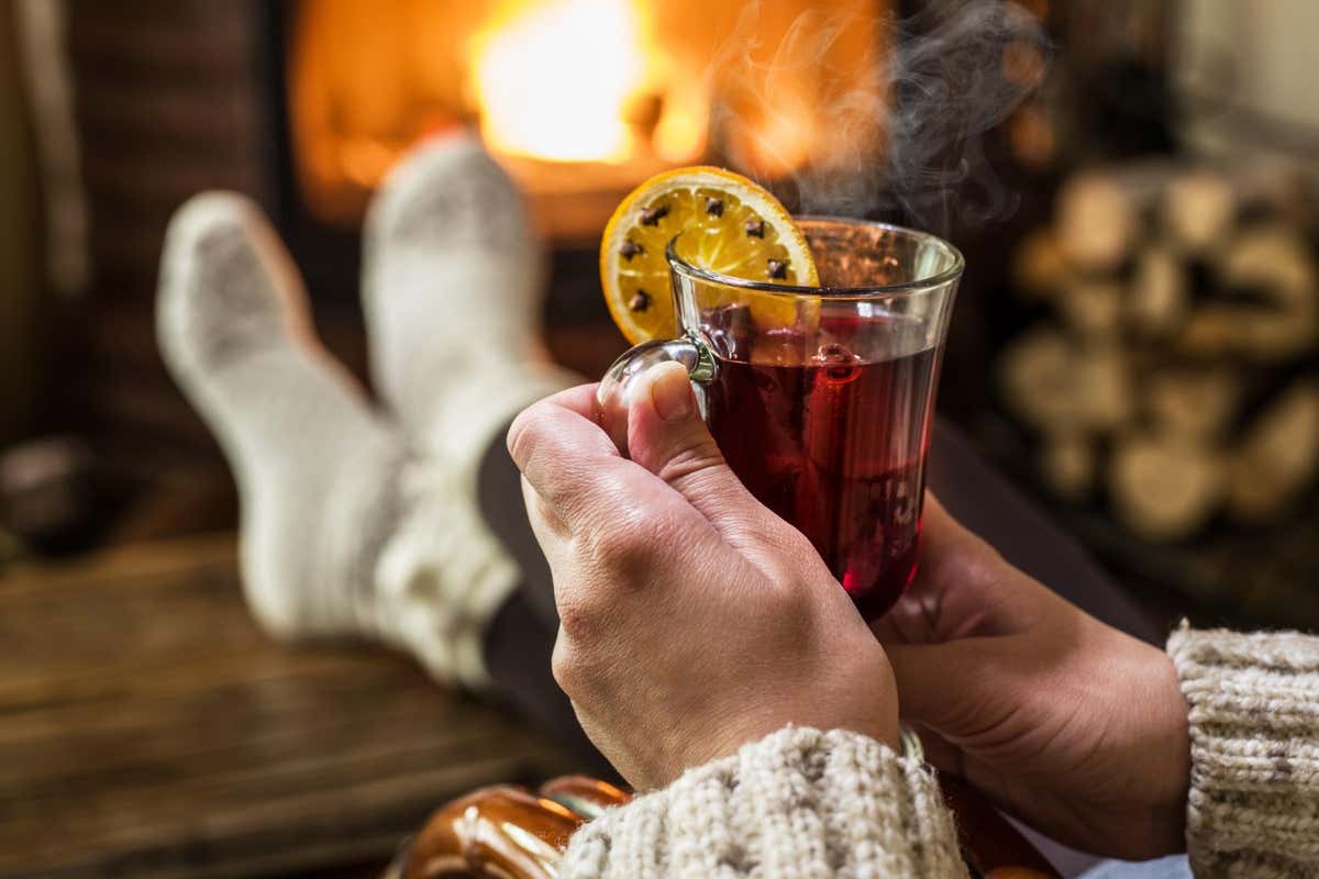 GTG9F9 Hot mulled wine and book in woman hands. Relaxing in front of burning fire in the cold winter day.